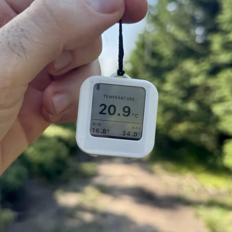Thermio v ruce na lesní stezce, displej ukazuje 20,9 °C